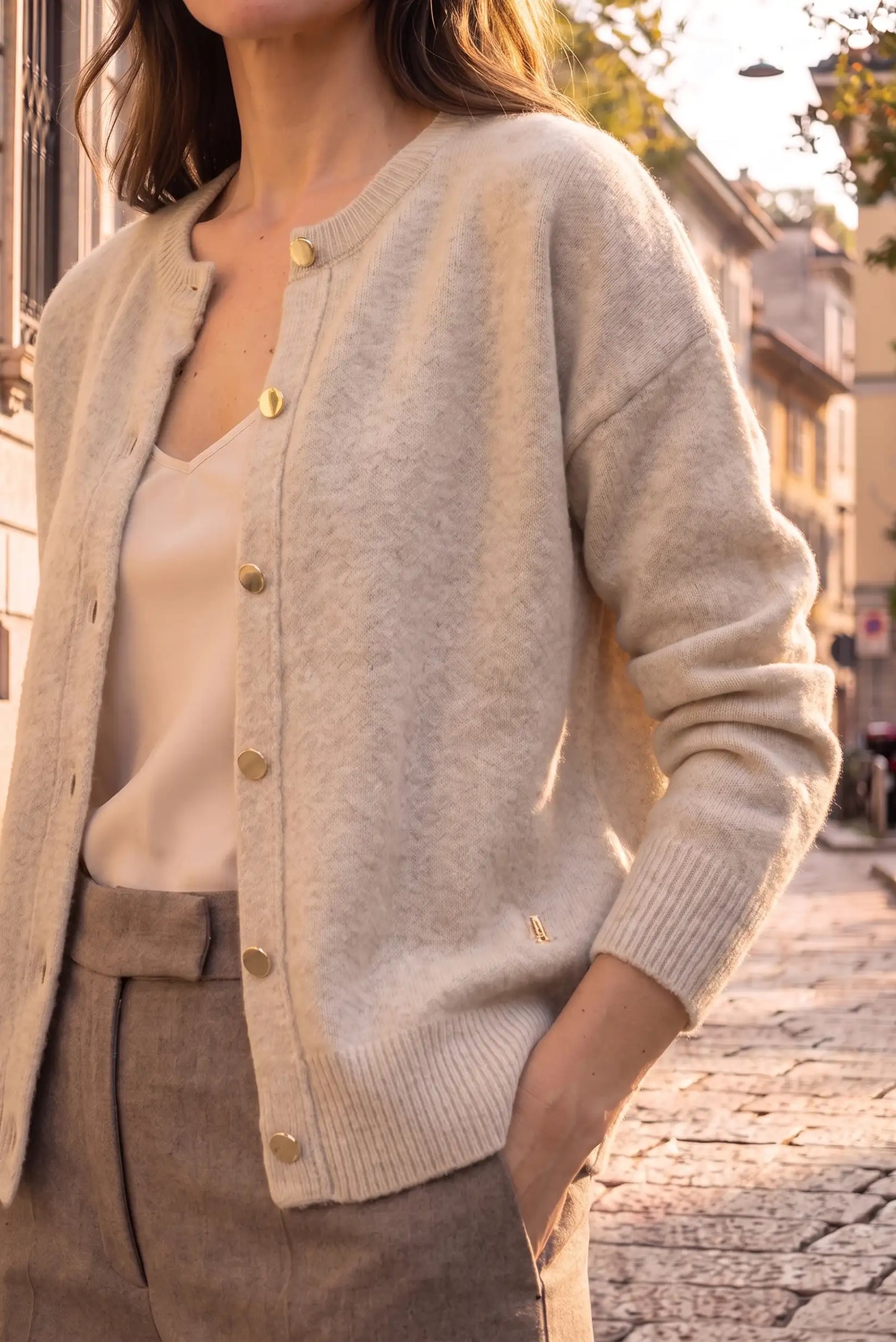 Mujer vistiendo rebeca de punto beige con botones dorados y pantalones marrón claro.