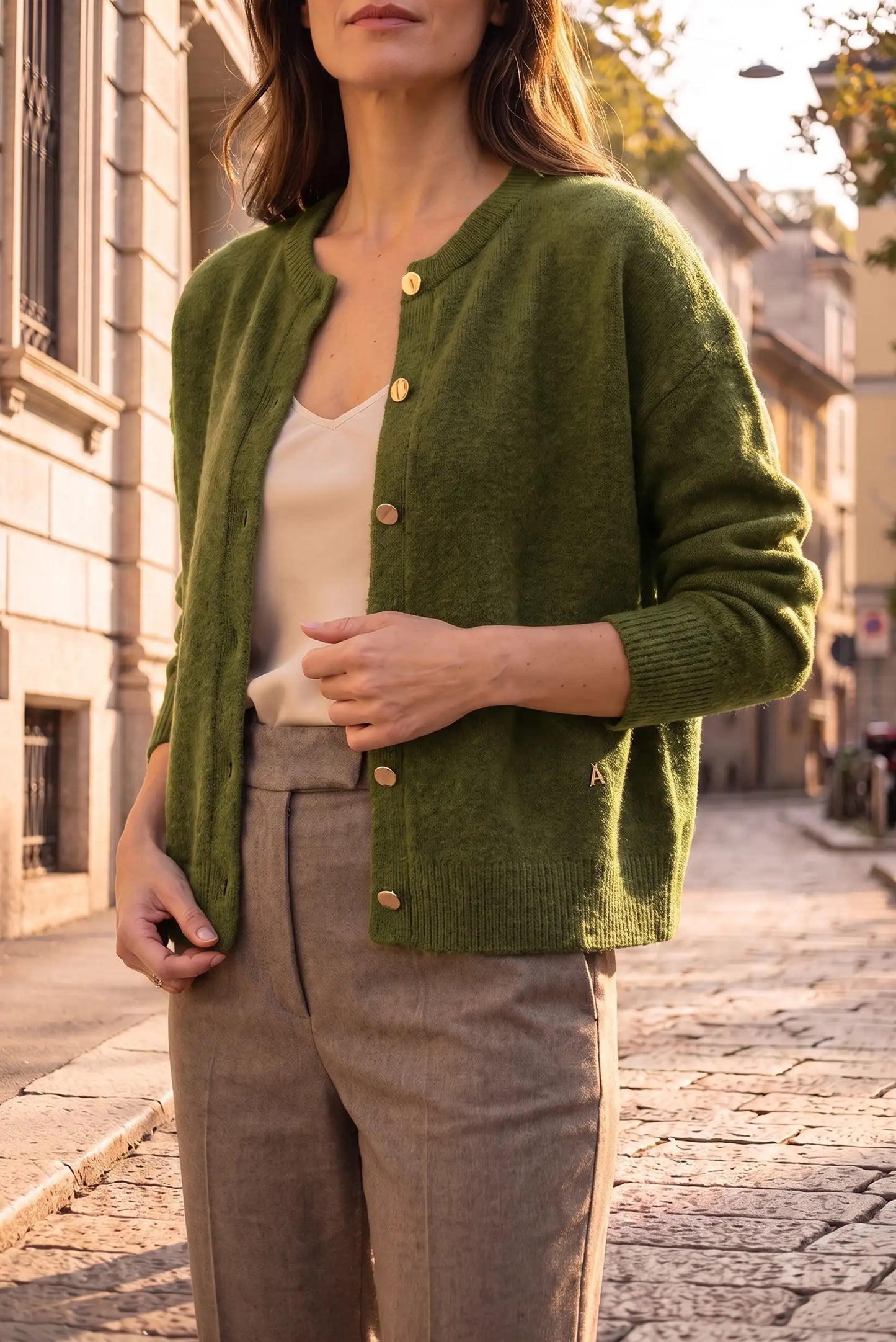 Mujer vistiendo una rebeca de punto verde oliva con botones dorados y pantalones beige.