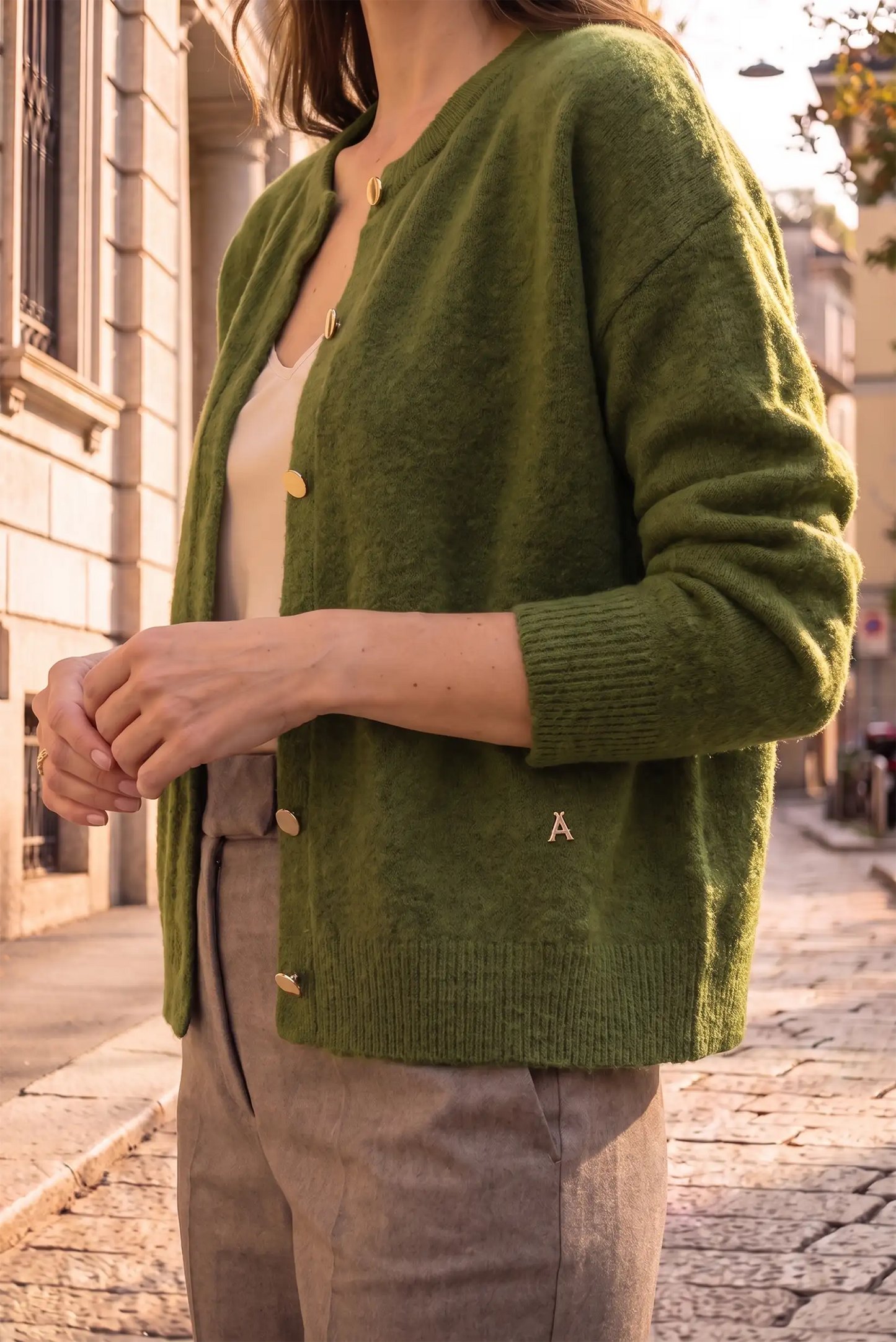 Mujer vistiendo una rebeca de punto en color verde con botones dorados y pantalones beige.
