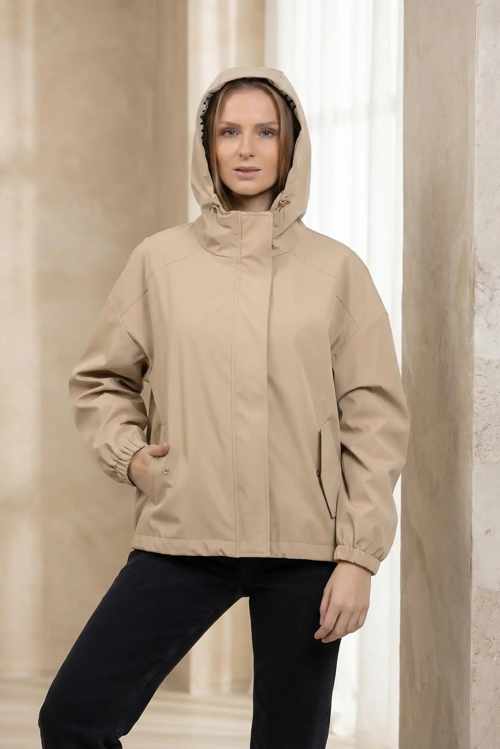 Chubasquero corto beige para mujer con capucha, estilo casual, fondo interior luminoso.