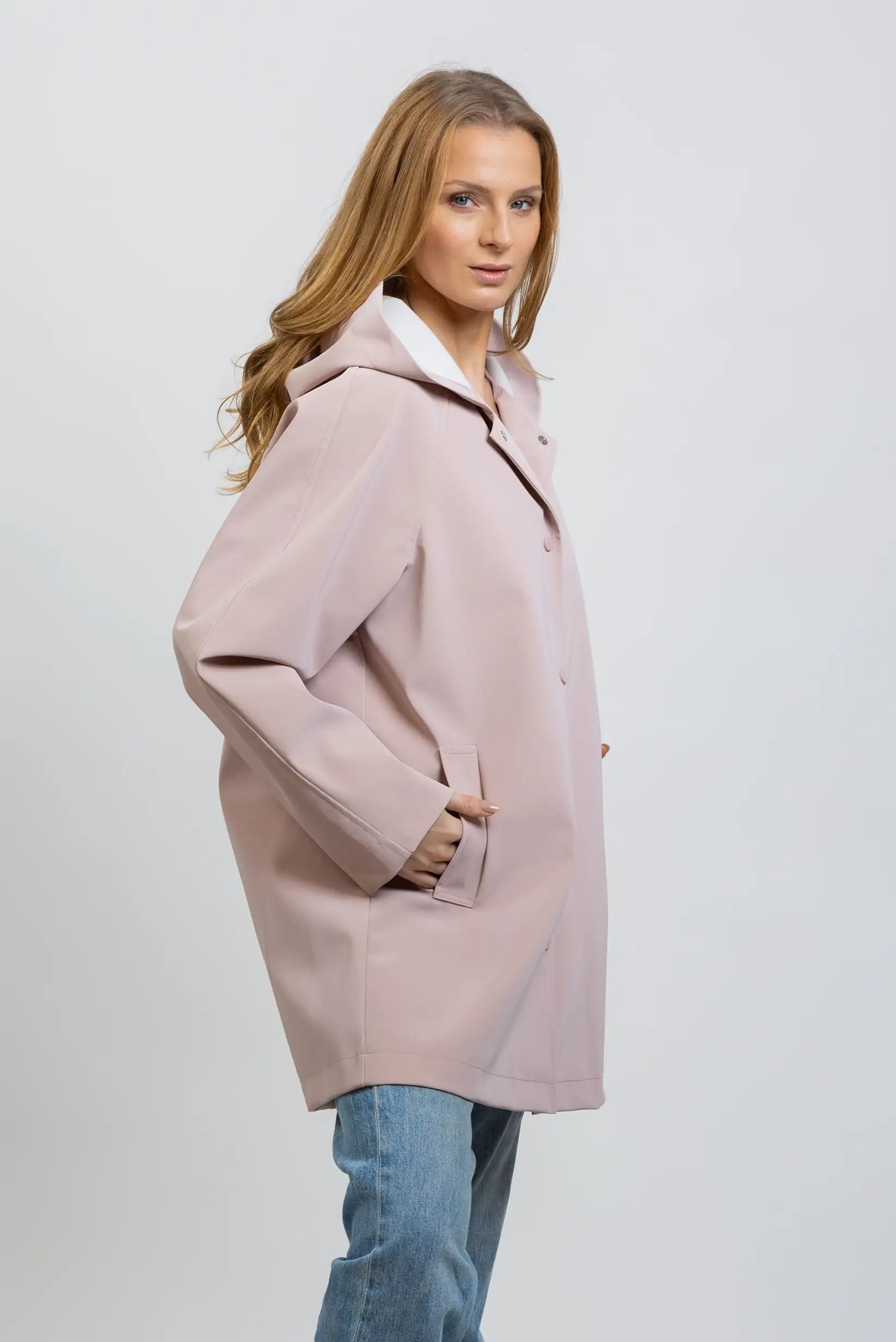 Mujer con chubasquero largo rosa empolvado, estilo casual, primavera, fondo neutro.