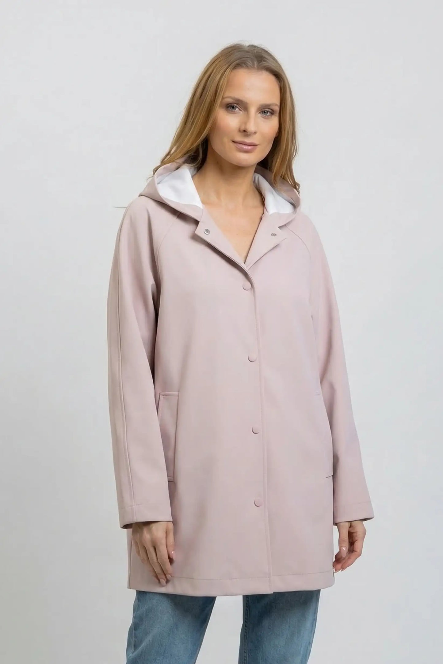 Mujer lleva chubasquero largo rosa empolvado con capucha, look casual de primavera.