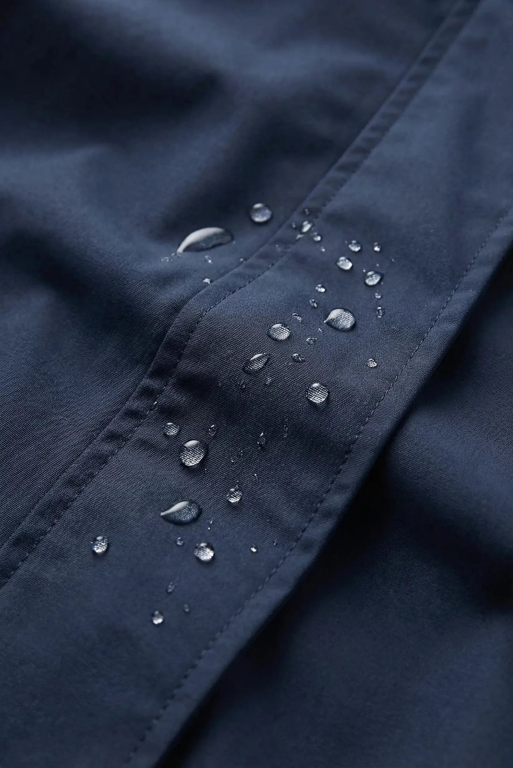 Detalle de chubasquero corto azul oscuro impermeable para mujer con gotas de agua, CHICA del Sur.