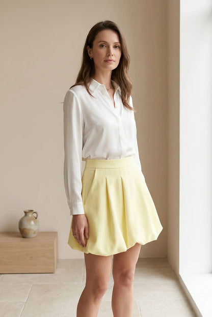 Mujer con falda globo corta amarilla y blusa blanca en ambiente minimalista
