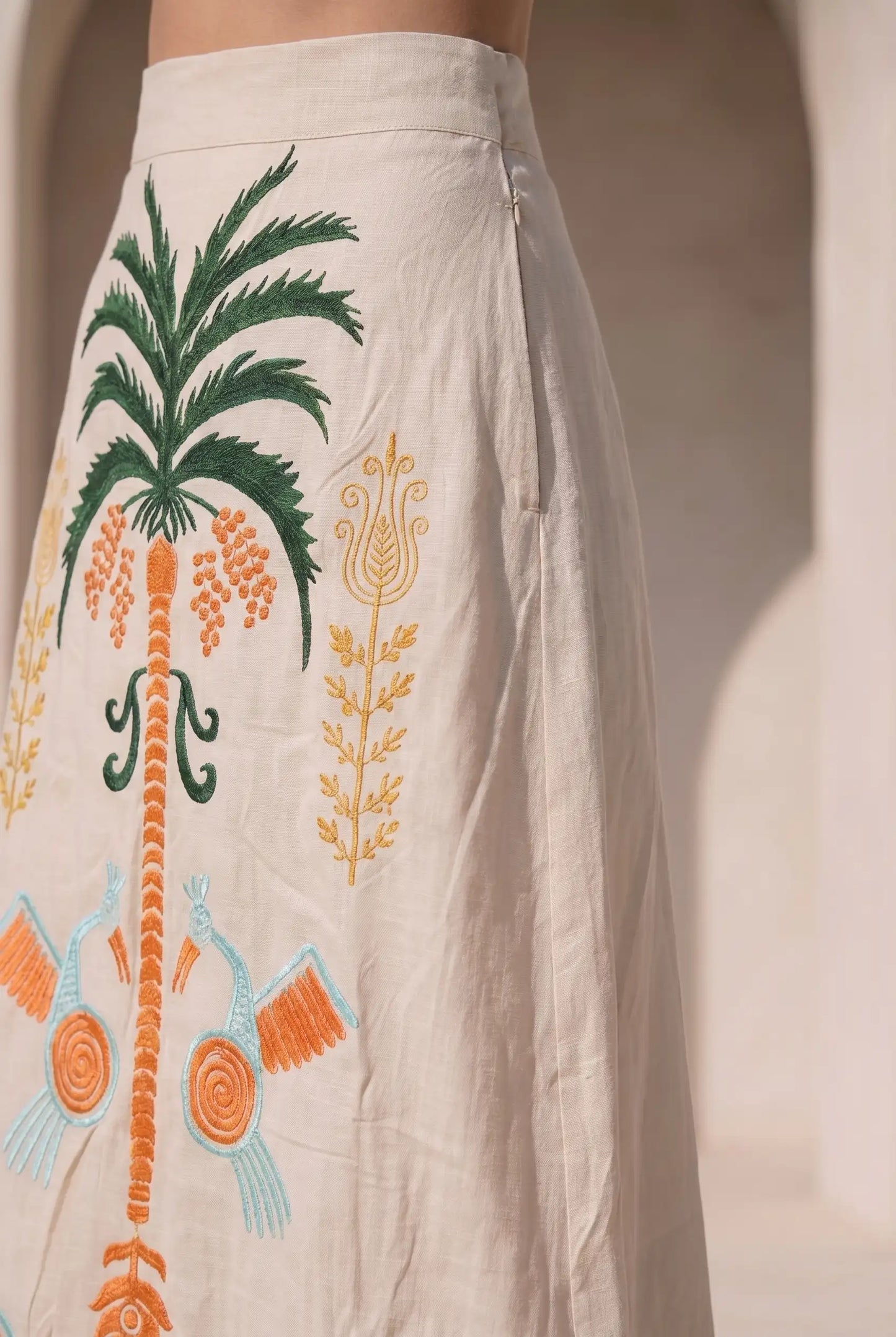 Falda larga beige con bordados tropicales en verde, naranja y azul, detalles de pájaros y palmera