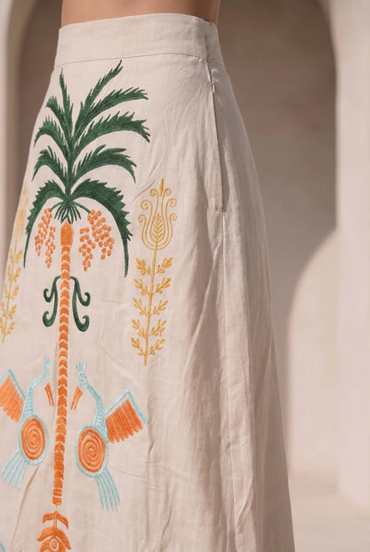 Falda larga beige con bordados tropicales en verde, naranja y azul, detalles de pájaros y palmera