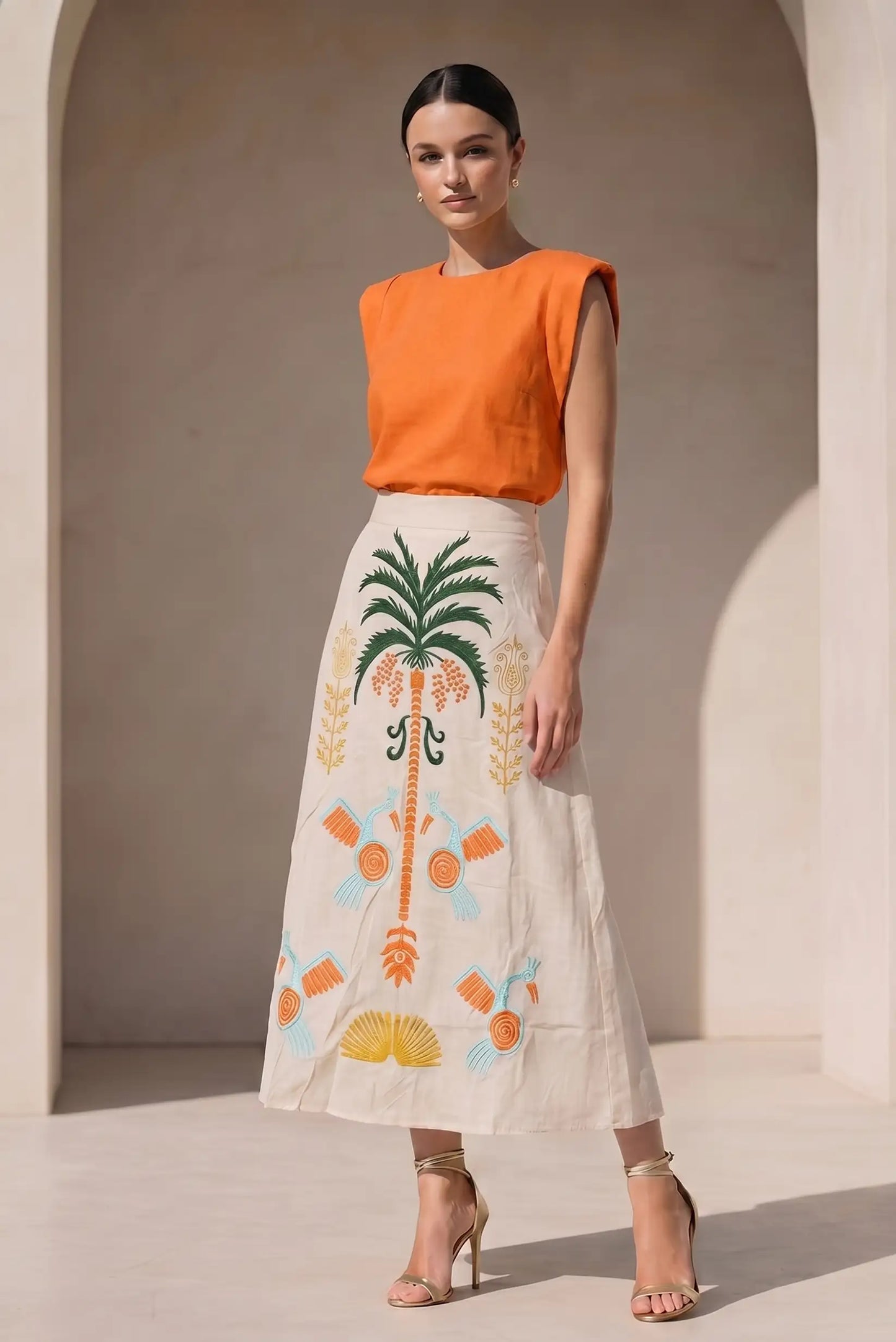 Falda larga beige con bordados tropicales en naranja, verde y azul, mujer con blusa naranja elegante