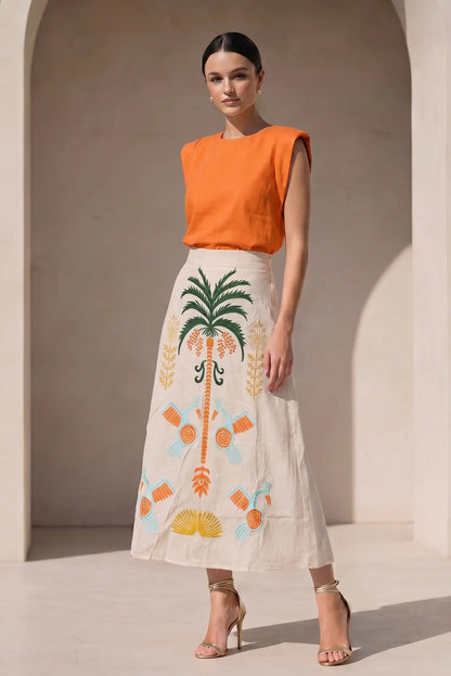Falda larga beige con bordados tropicales en naranja, verde y azul, mujer con blusa naranja elegante
