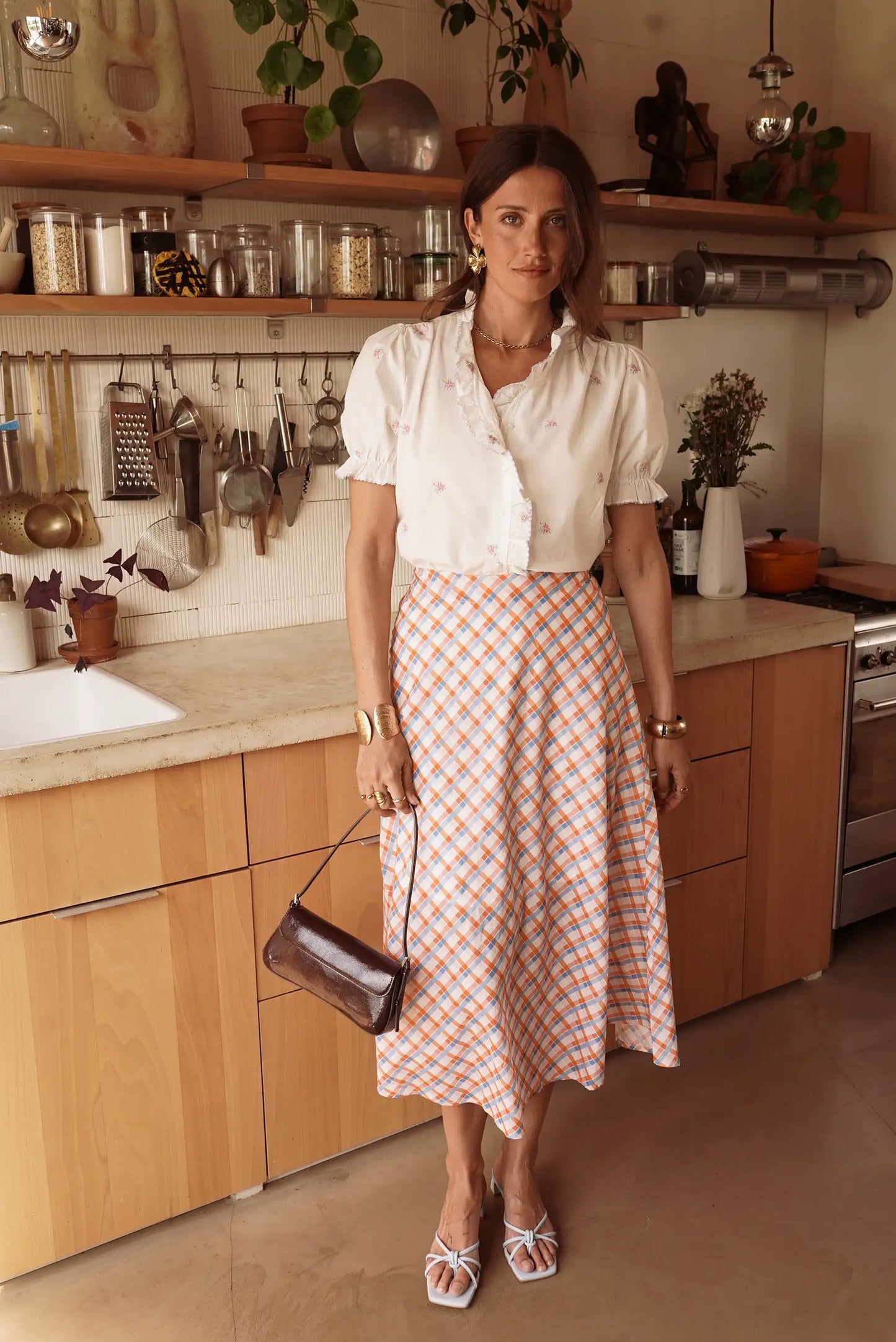 Mujer con falda larga de cuadros vichy naranja y azul, blusa blanca, en cocina moderna