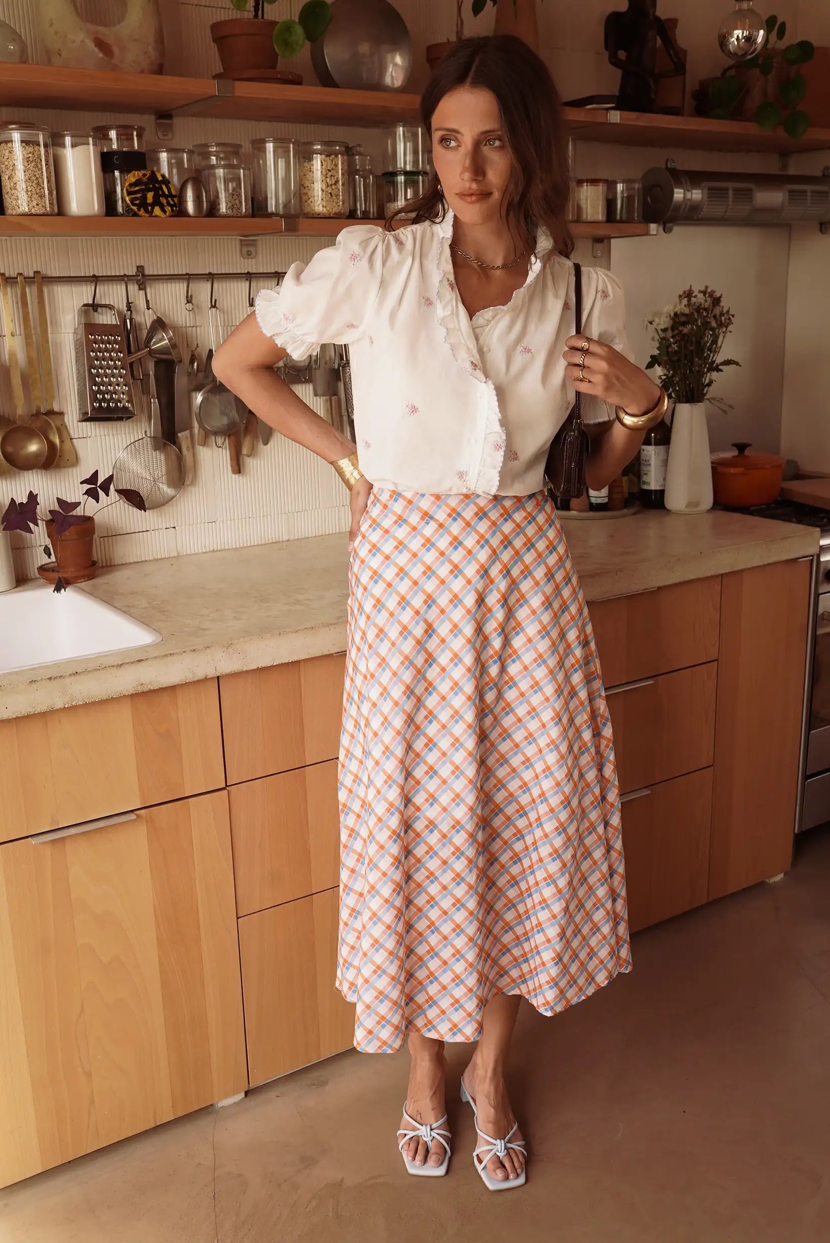 Mujer con falda larga de cuadros vichy naranja y azul, blusa blanca, en cocina moderna.