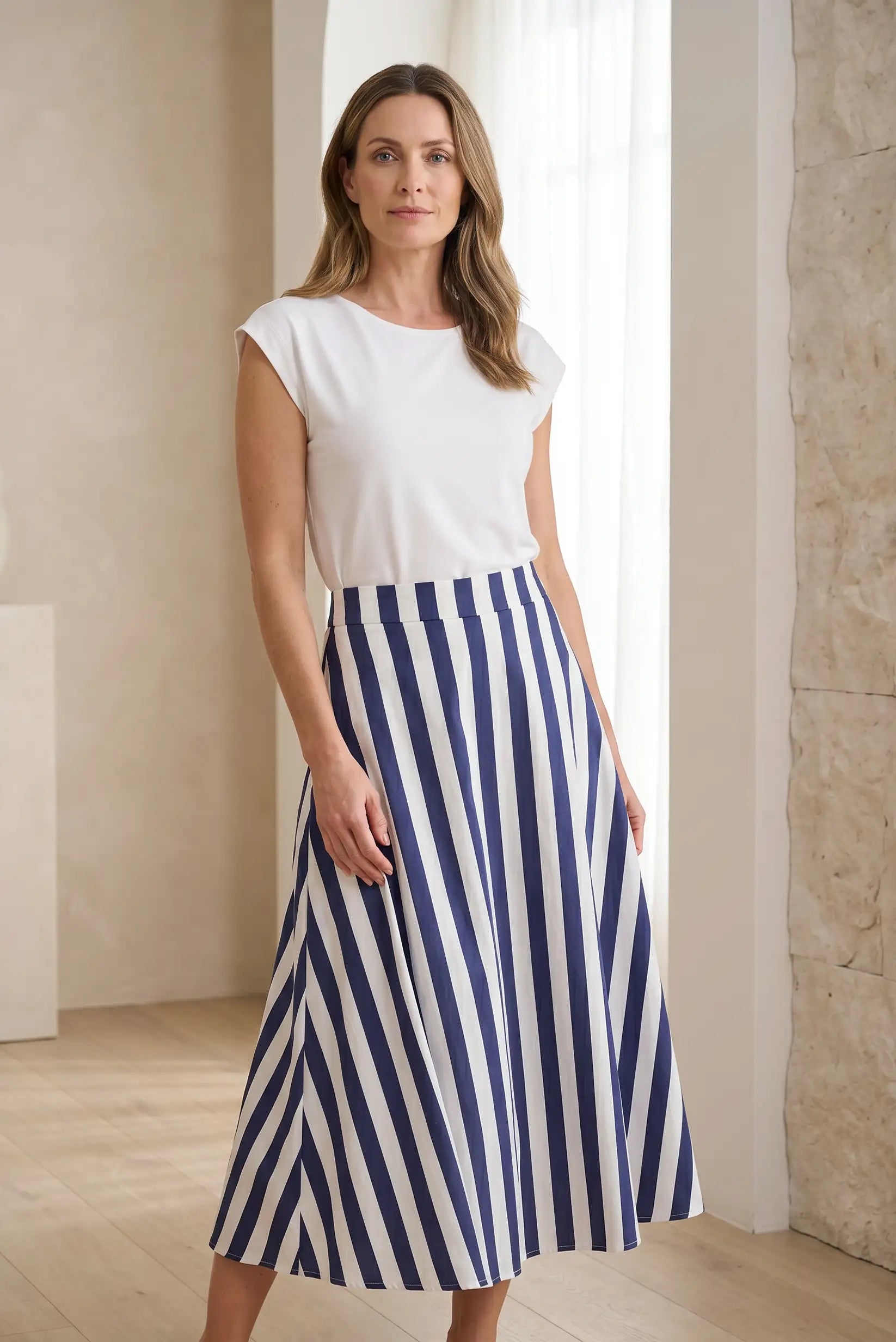 Mujer con falda larga de rayas azul y blanco y camiseta blanca en ambiente luminoso