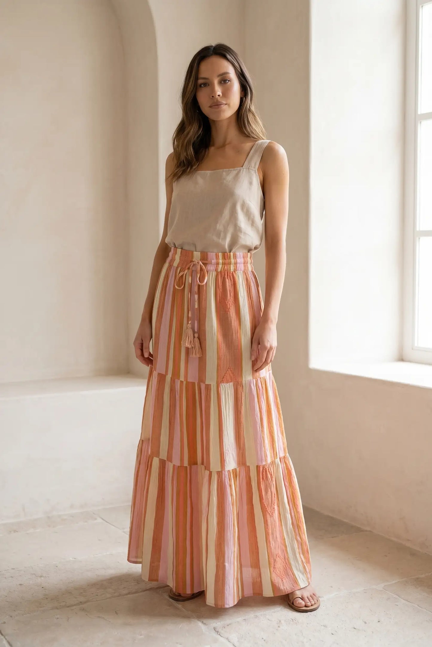 Mujer con falda larga de rayas naranjas y blusa beige en ambiente luminoso de primavera