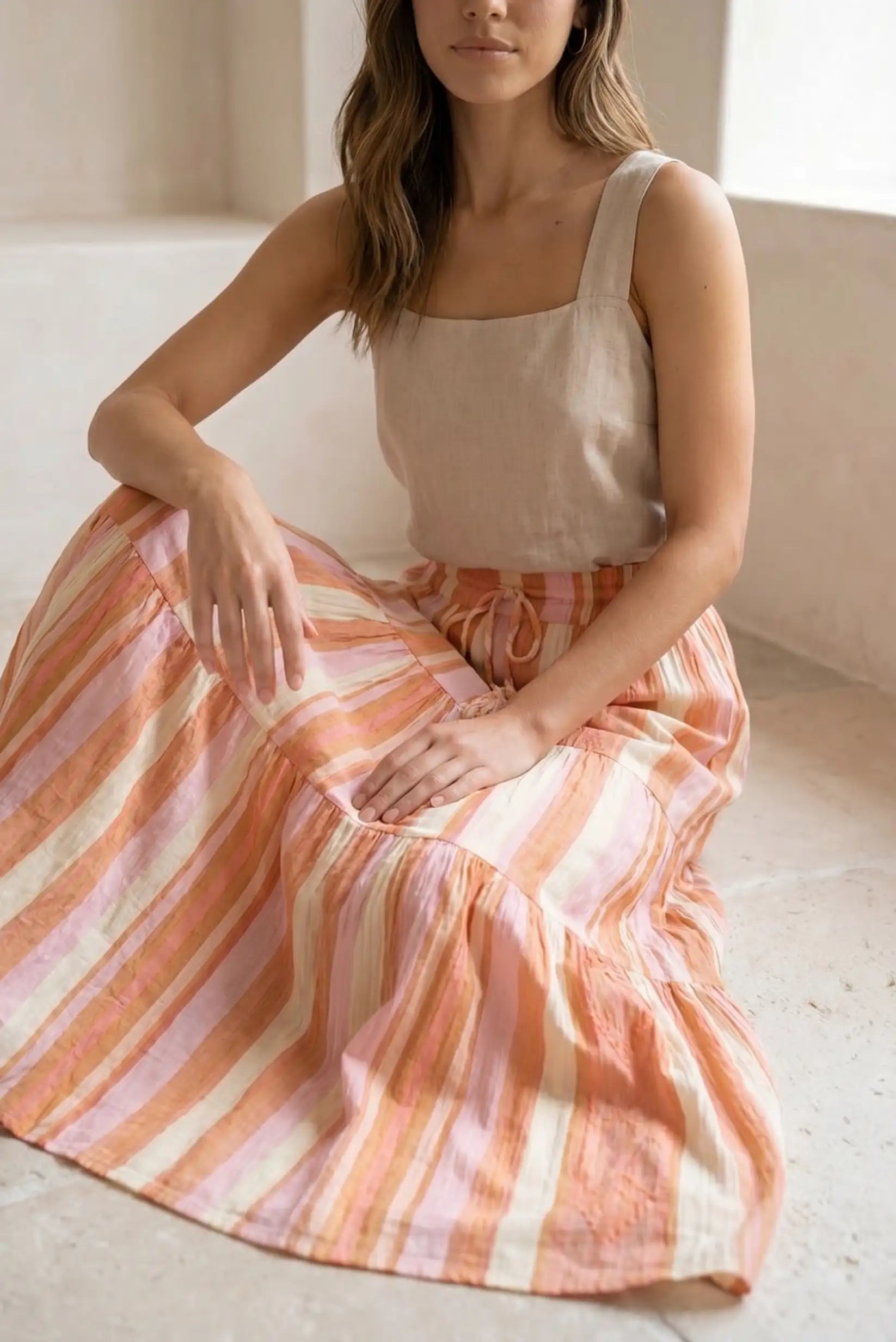 Mujer sentada con falda larga de rayas naranjas y rosas, blusa beige, estilo casual primavera