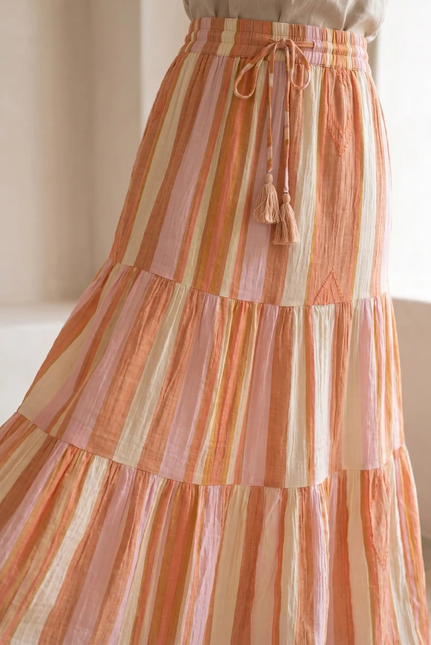 Falda larga de rayas en tonos naranjas y beige, con cinturón ajustable y textura ligera.