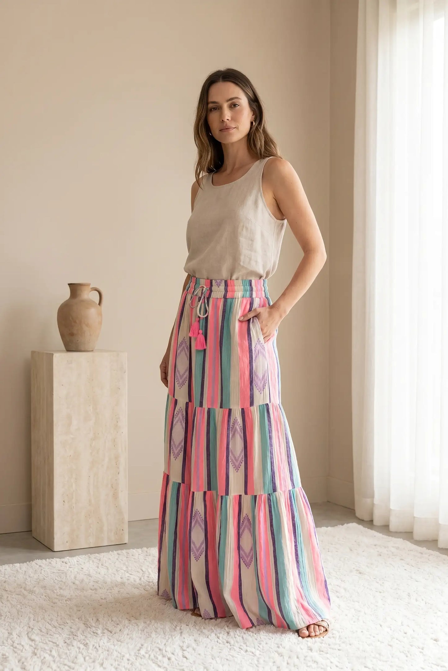 Mujer con falda larga de rayas rosas y top beige, look casual y primaveral en interior luminoso.