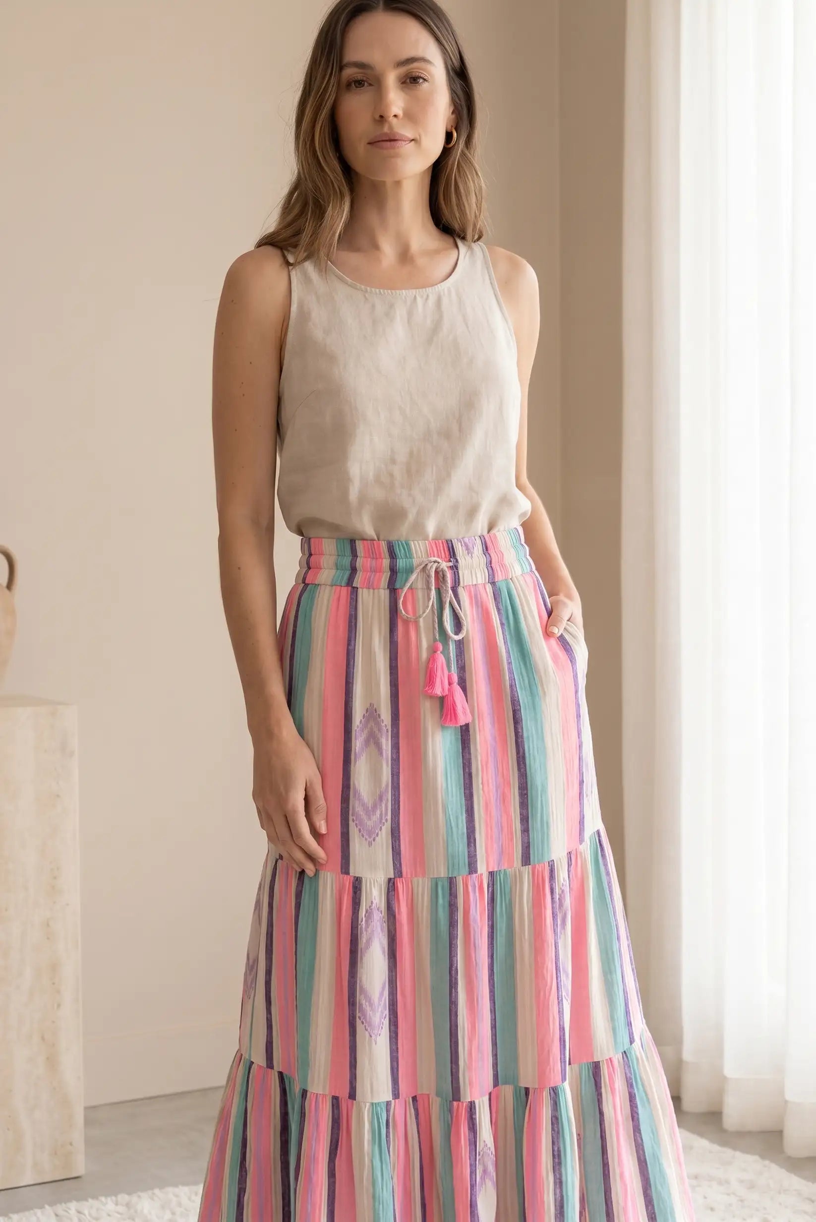 Mujer con falda larga de rayas rosas y top beige, look casual de primavera en interior luminoso.