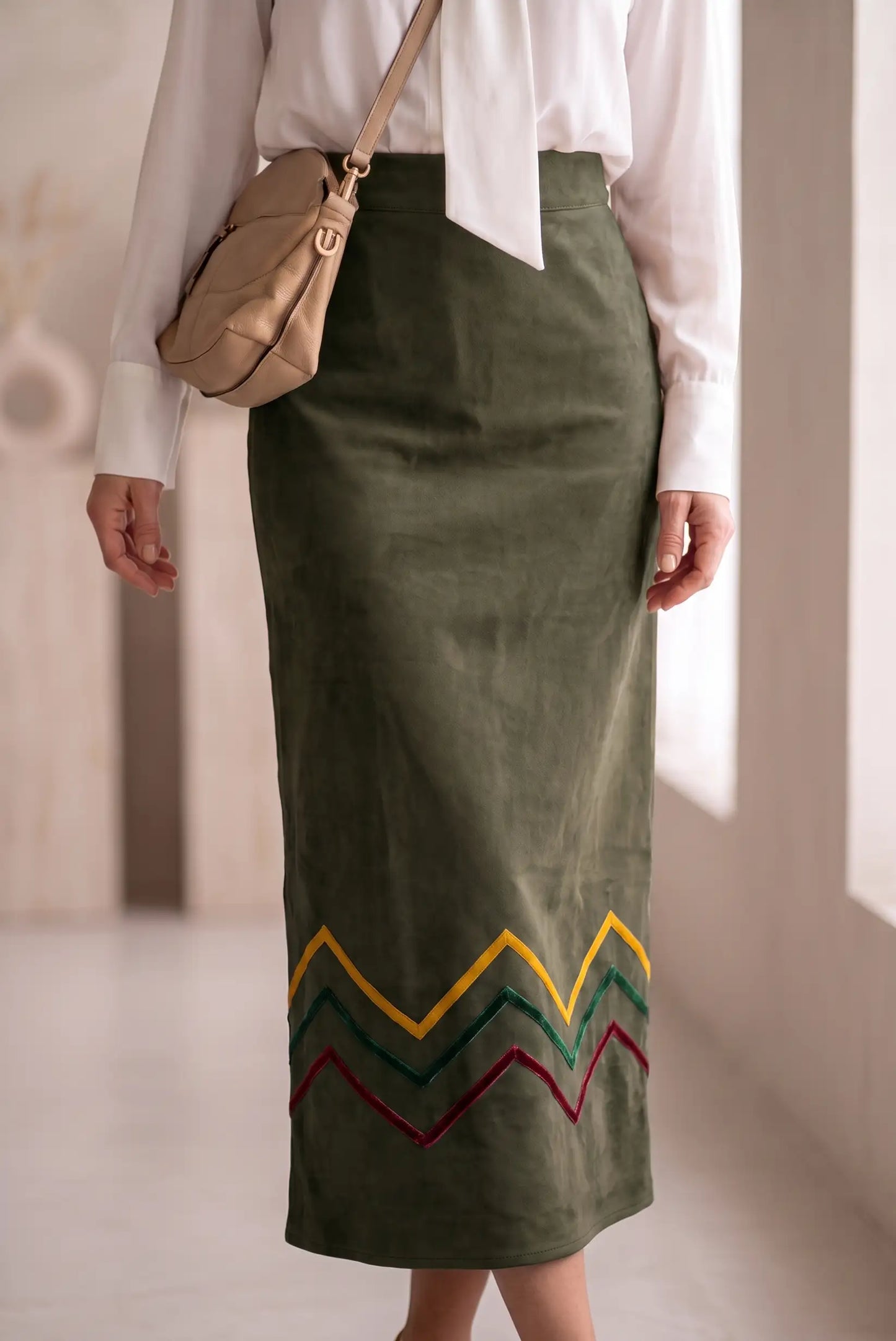 Mujer vistiendo falda midi verde oliva con bordado geométrico colorido y camisa blanca.