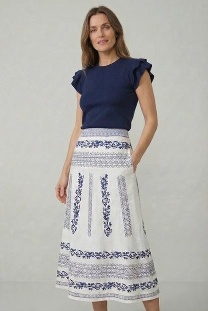 Mujer con blusa azul marino y falda blanca midi bordada con estampado azul, moda femenina casual.