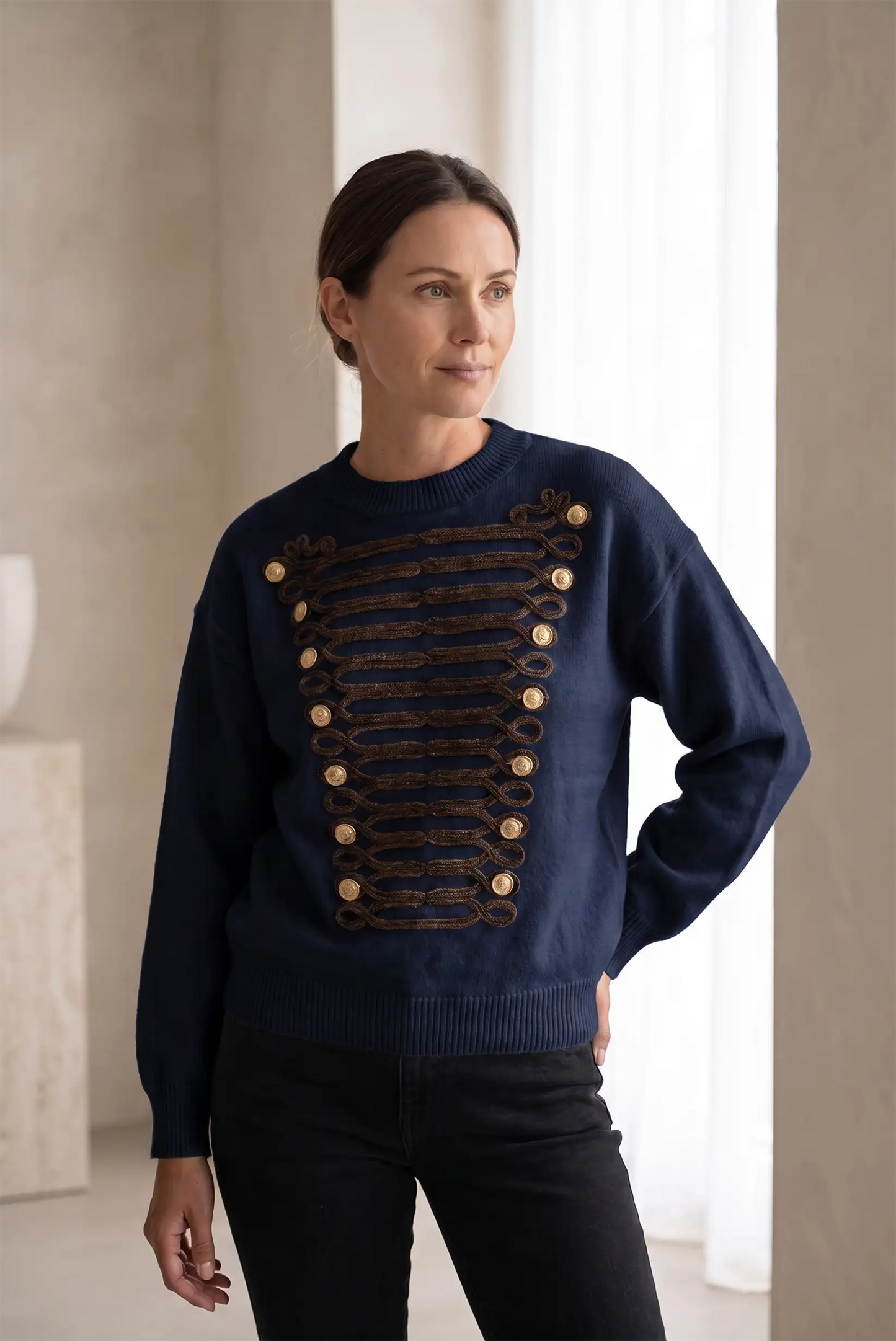 Mujer vistiendo jersey azul marino con detalles decorativos dorados y botones frontales.