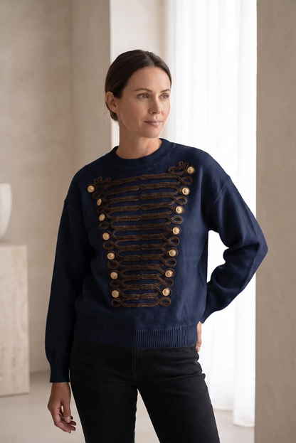 Mujer vistiendo jersey azul marino con detalles decorativos dorados y botones frontales.