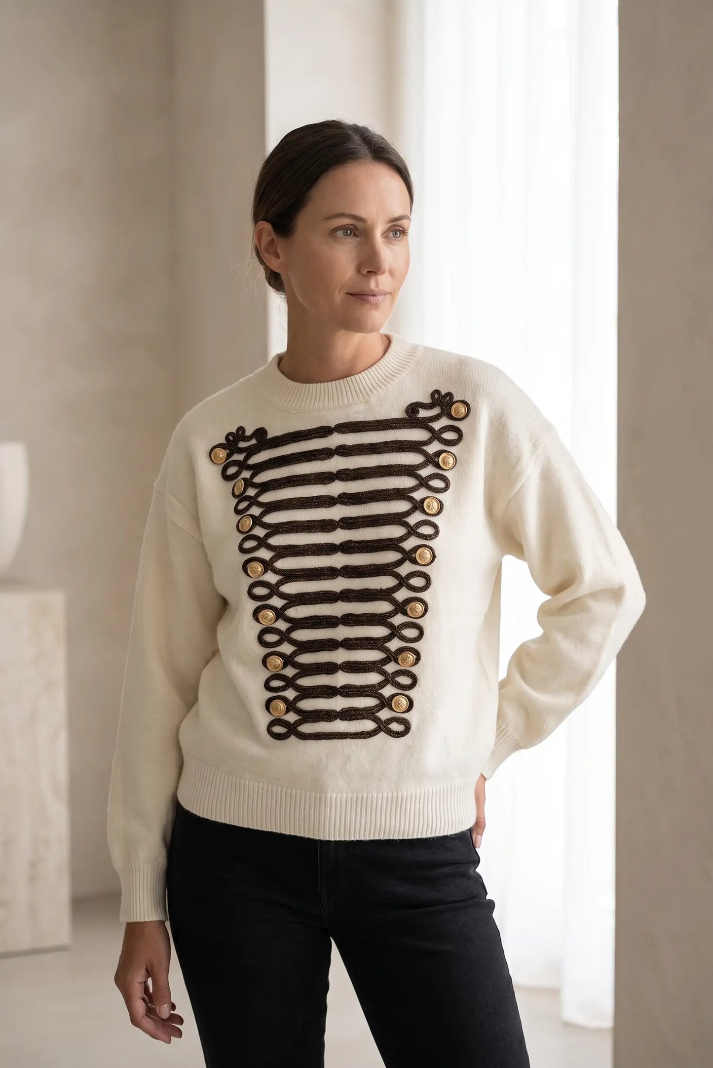Mujer vistiendo jersey blanco con detalles de alamares negros y botones dorados