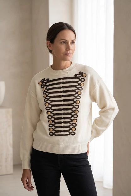 Mujer vistiendo jersey blanco con detalles de alamares negros y botones dorados