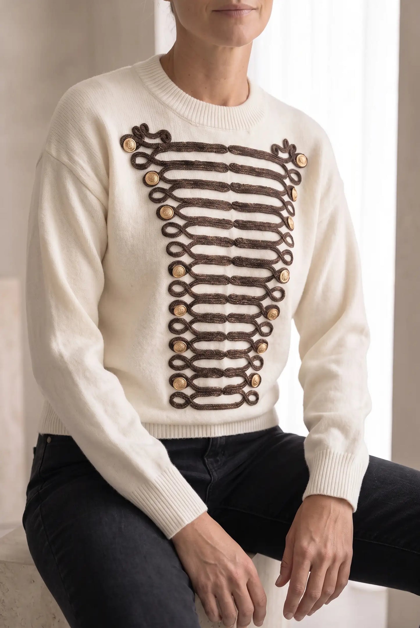 Jersey blanco para mujer con detalles de trenzado marrón y botones dorados estilo militar.