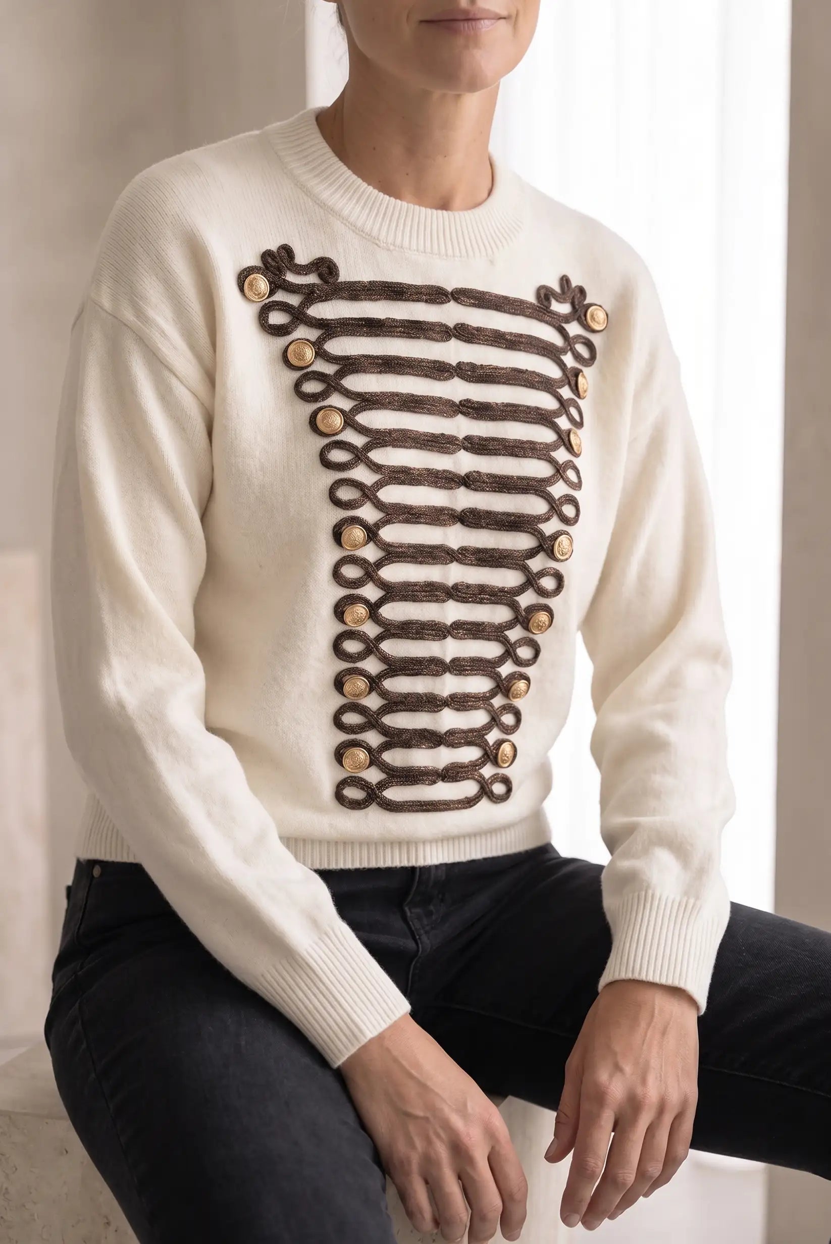 Jersey blanco para mujer con detalles de trenzado marrón y botones dorados estilo militar.