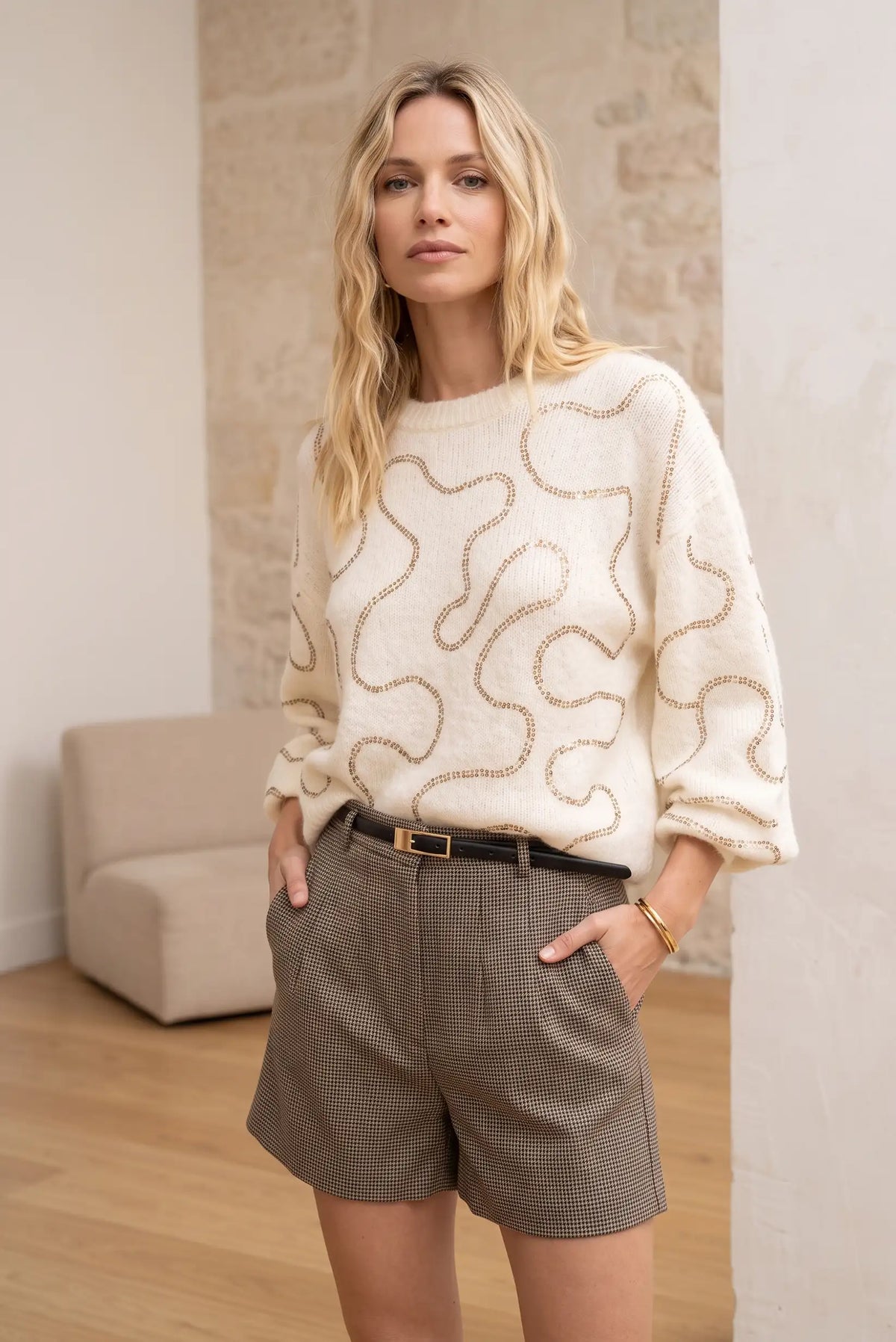 Mujer vistiendo jersey beige con abalorios dorados y shorts a cuadros de CHICA del Sur.