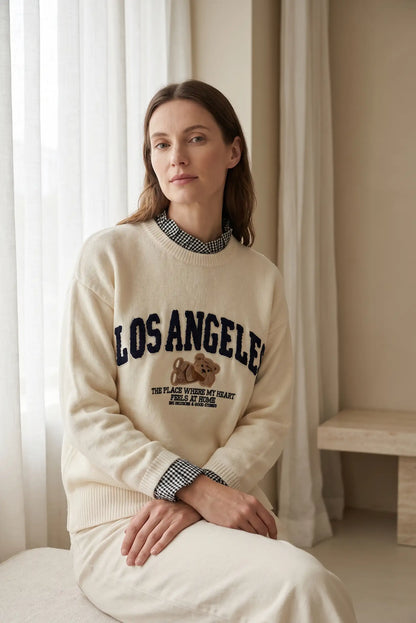 Mujer vistiendo jersey beige de CHICA del Sur con bordado de Los Angeles y un osito.