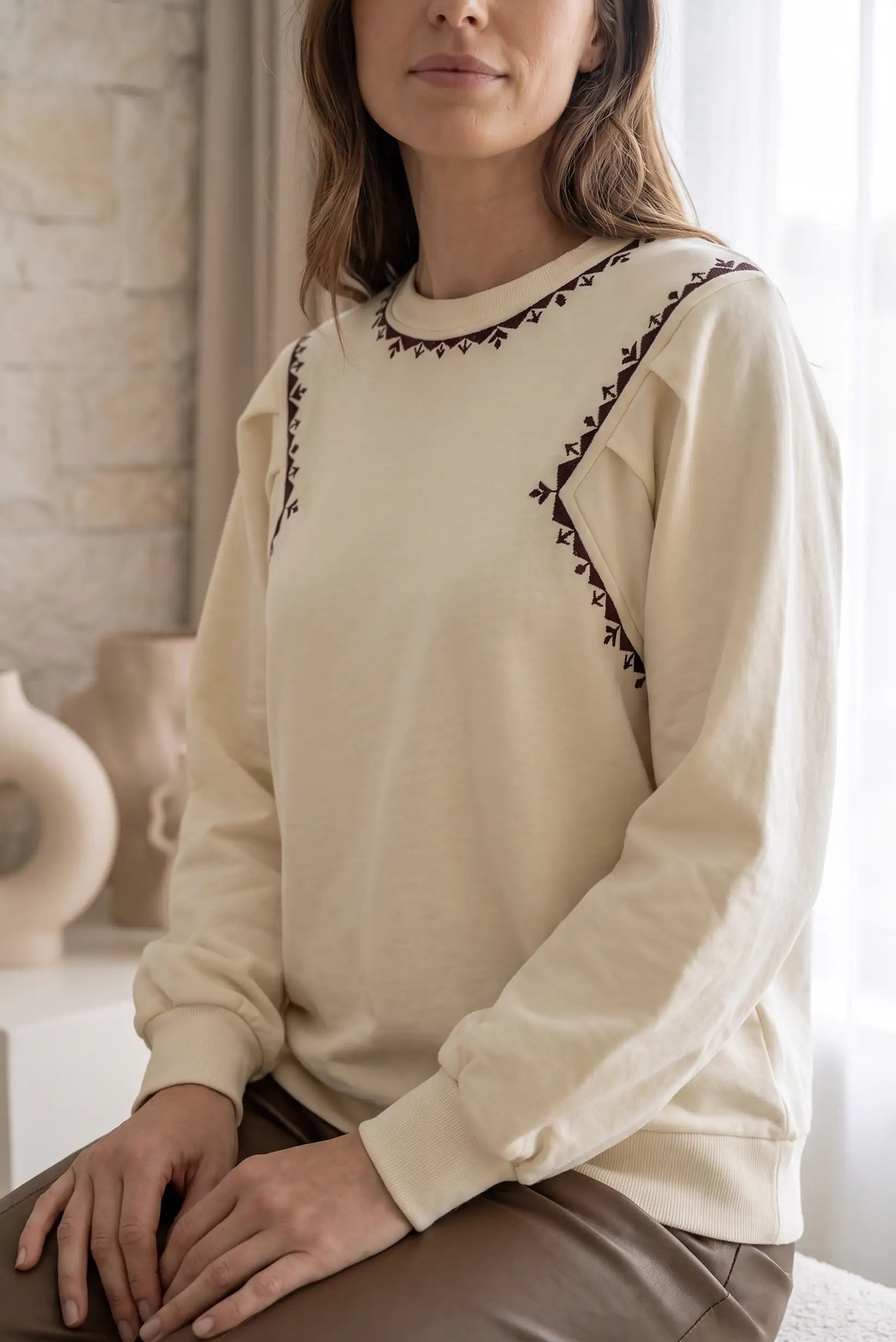 Mujer vistiendo sudadera beige con bordados decorativos en color granate.