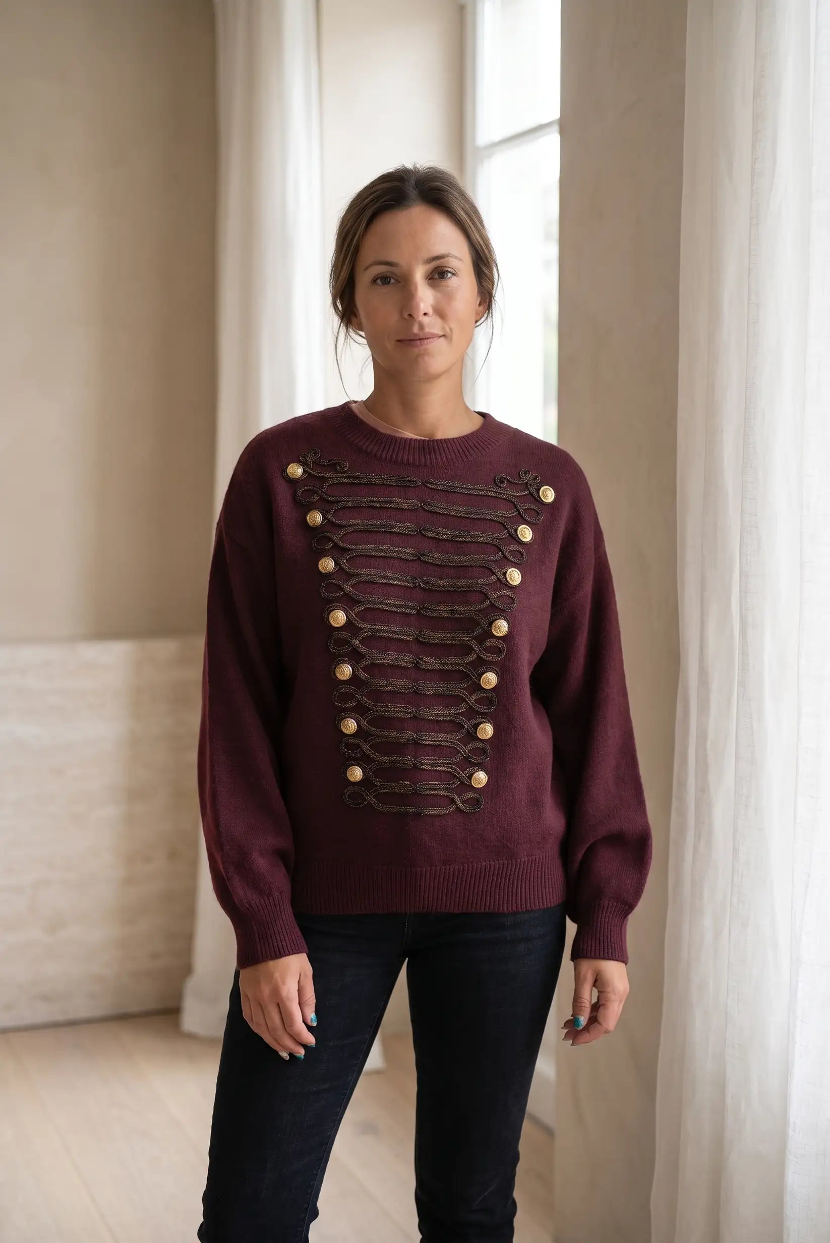 Mujer con jersey granate de estilo militar con botones dorados y detalles trenzados.