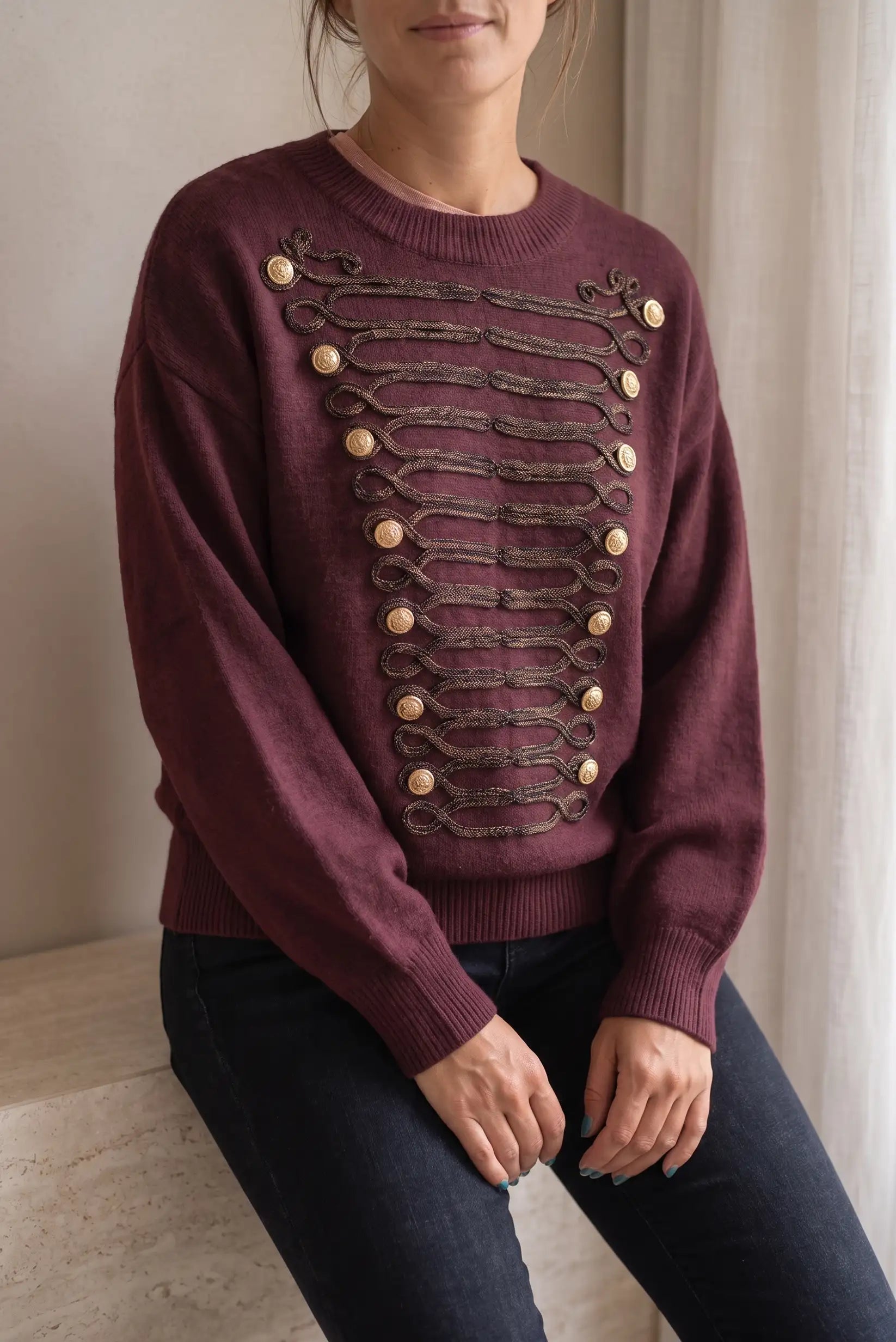 Jersey granate de punto con detalles de botones dorados y cordones ornamentales.