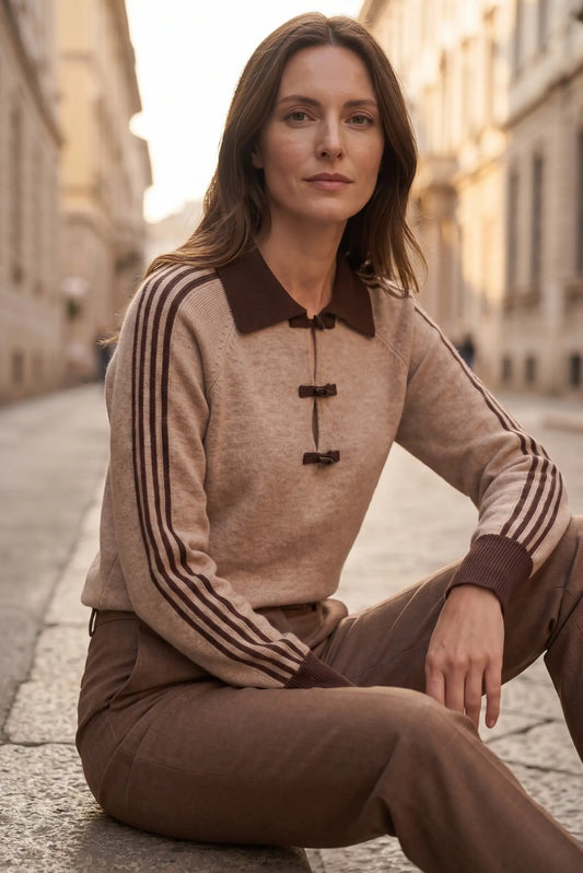 Mujer con jersey beige de cuello marrón y pantalones marrones en una calle europea.