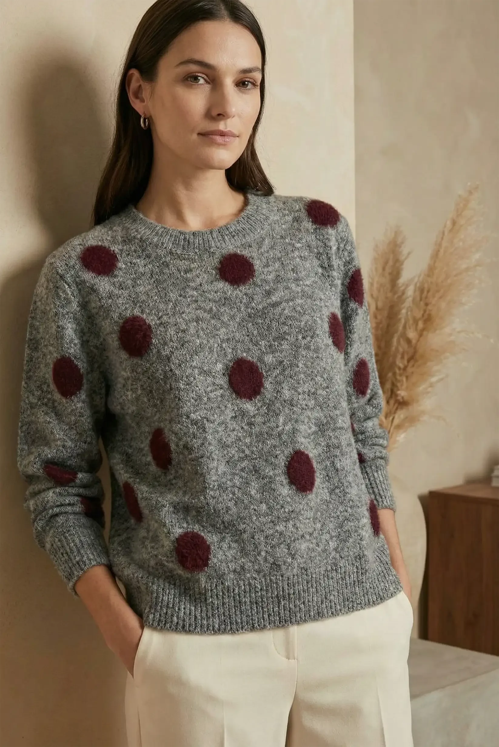 Mujer con jersey gris de punto con lunares burdeos, pantalón claro, ambiente interior minimalista