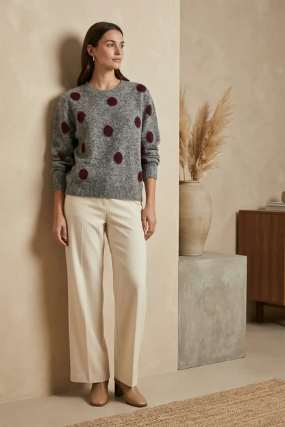 Mujer con jersey gris de lunares burdeos y pantalones beige en ambiente minimalista