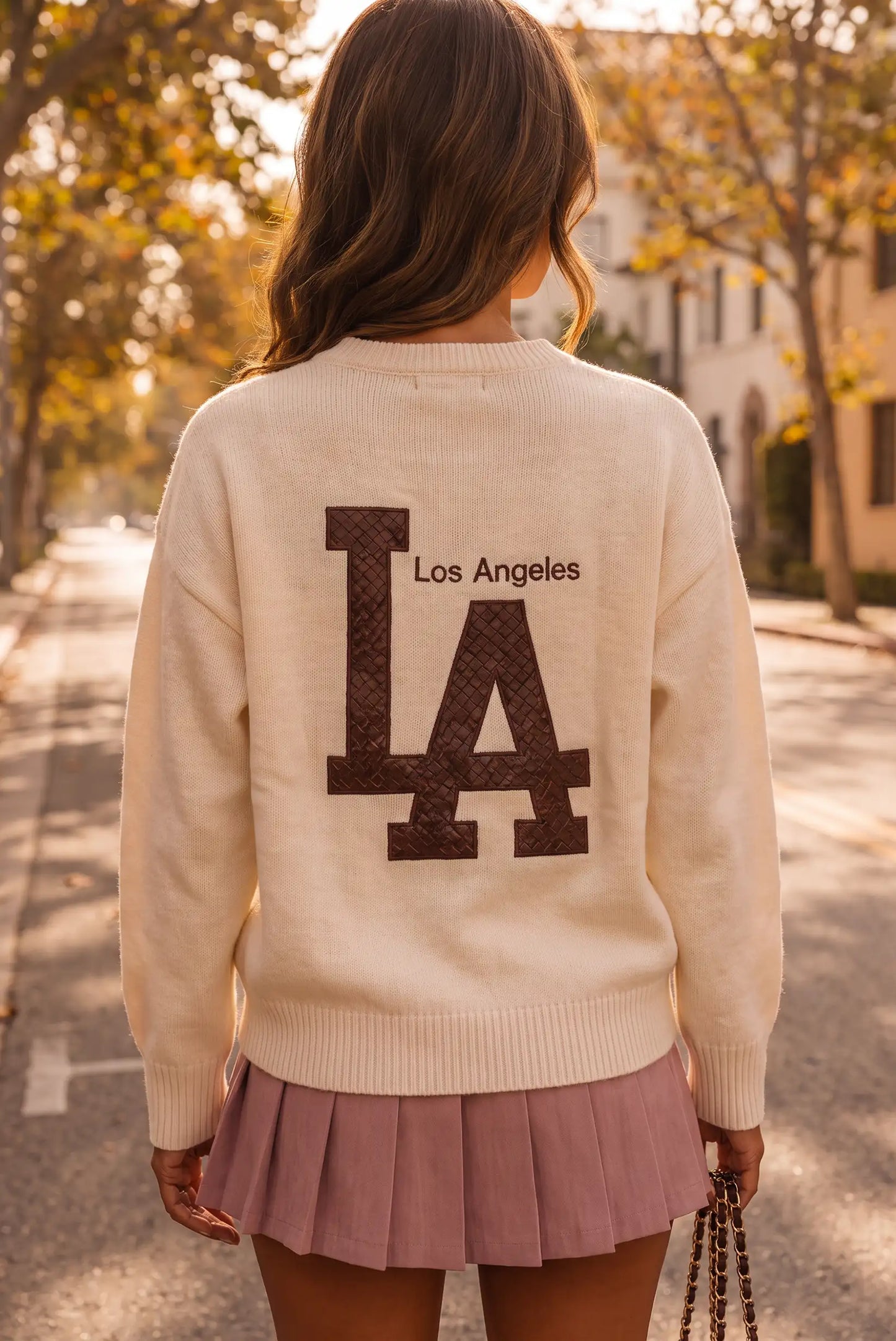 Mujer de espaldas con jersey crema con logo de Los Angeles y falda plisada rosa.
