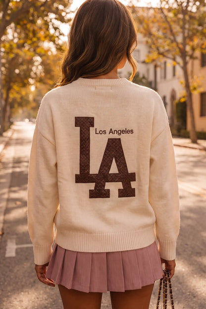Mujer de espaldas con jersey crema con logo de Los Angeles y falda plisada rosa.