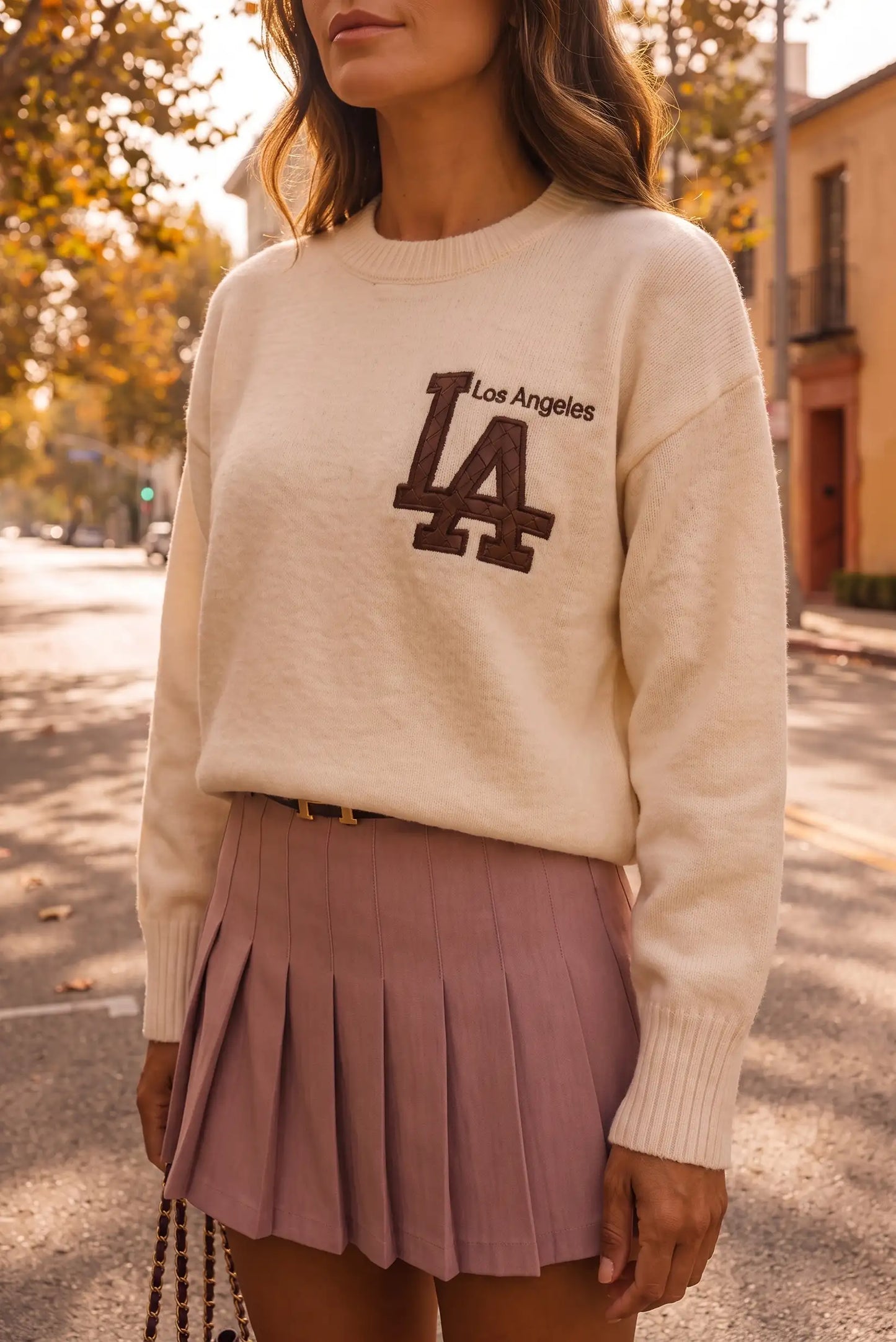 Mujer con jersey beige de Los Angeles y falda plisada color malva en entorno urbano.