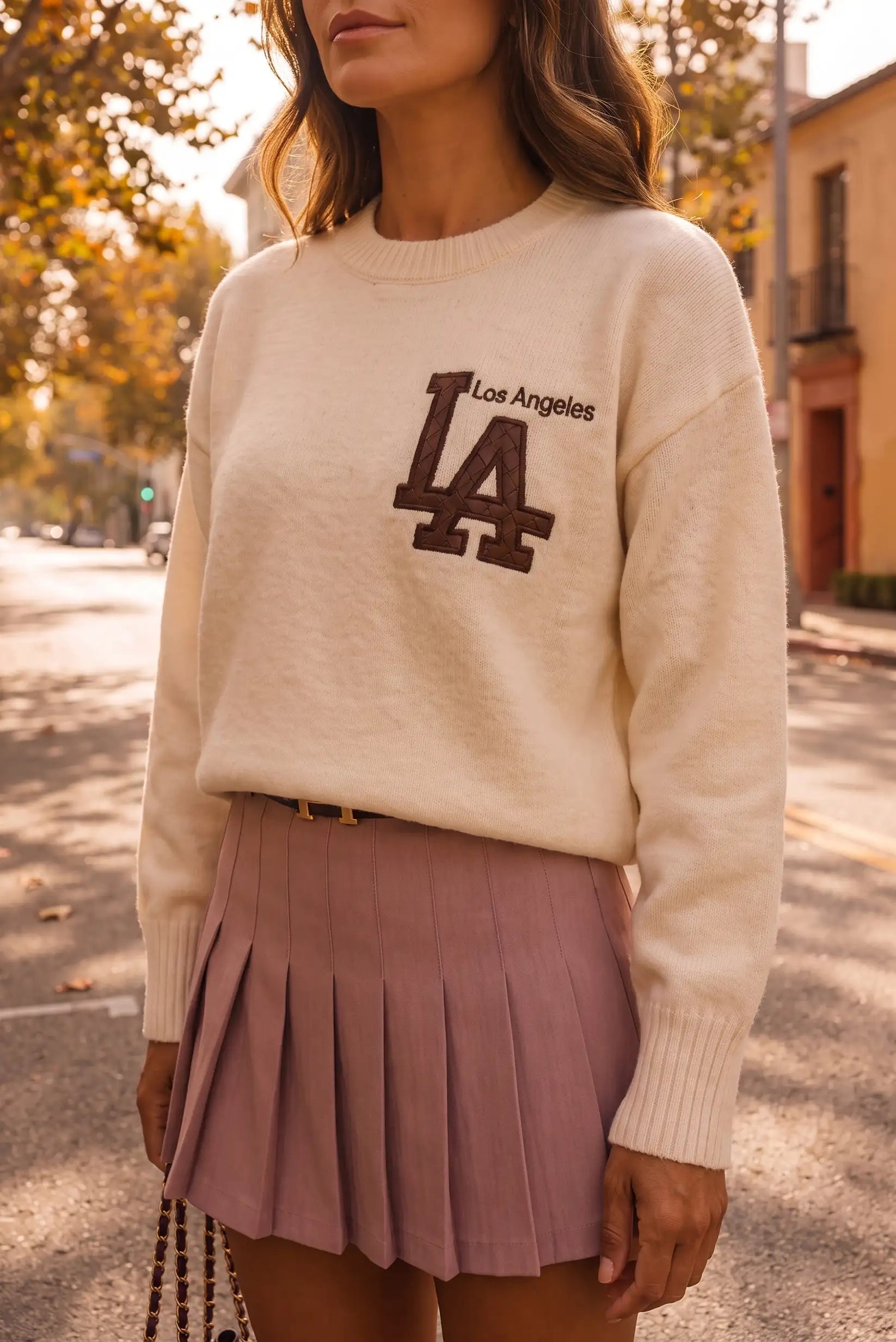 Mujer con jersey beige de Los Angeles y falda plisada color malva en entorno urbano.