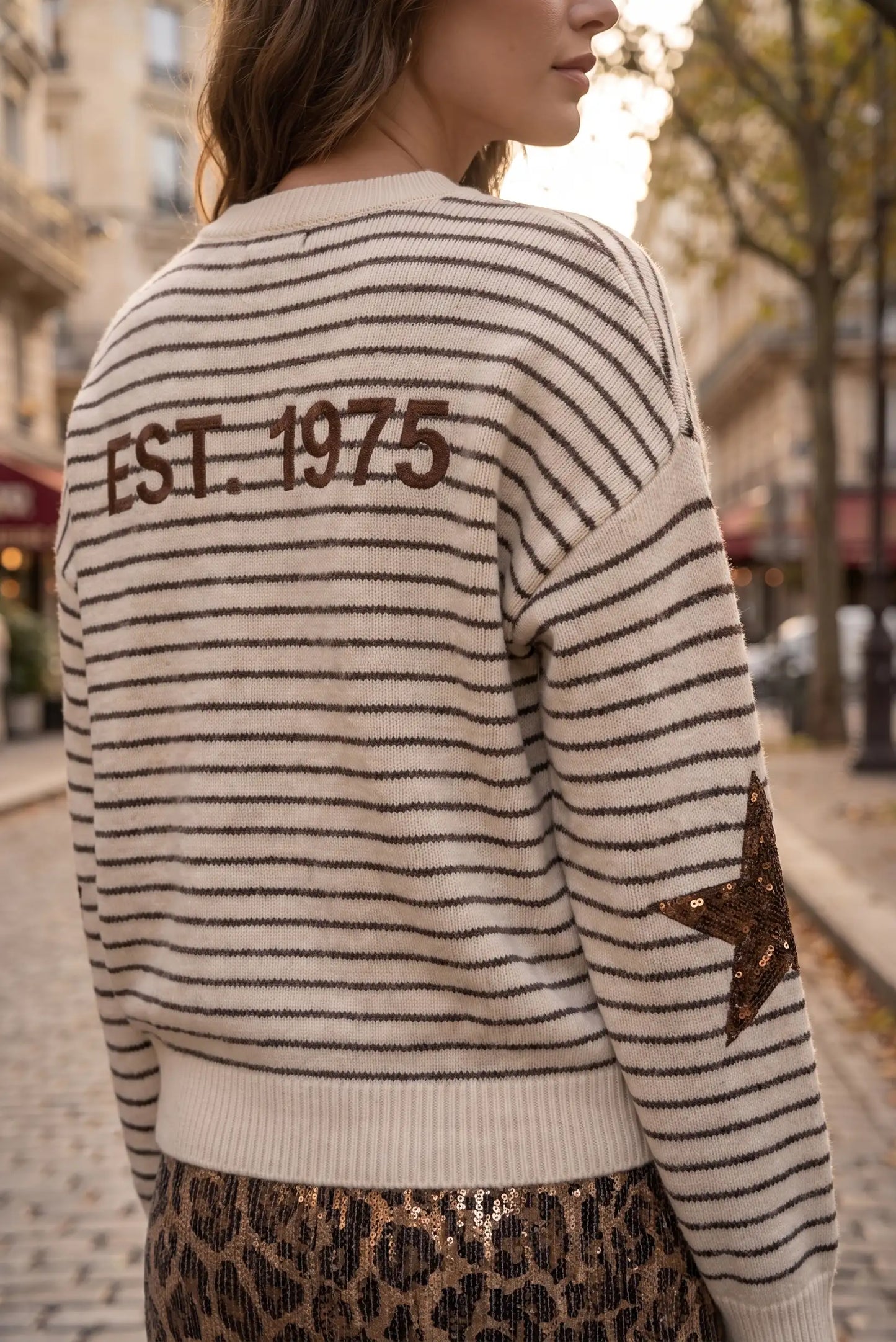 Jersey de rayas beige y marrón con texto 'EST. 1975' y estrella de lentejuelas en la manga