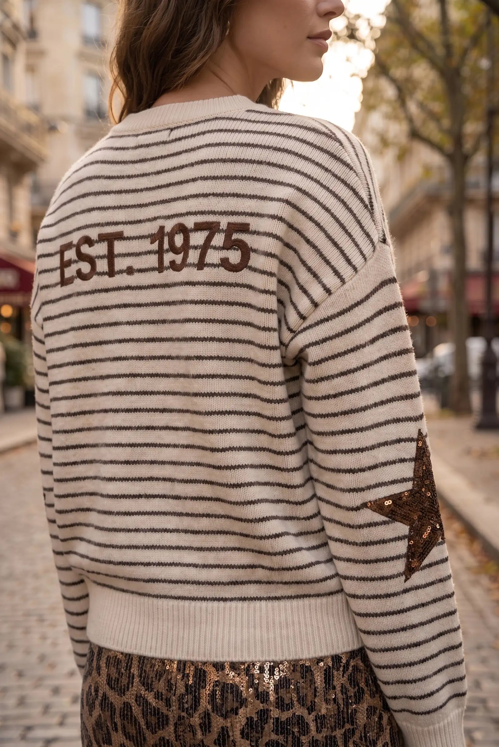 Jersey de rayas beige y marrón con texto 'EST. 1975' y estrella de lentejuelas en la manga