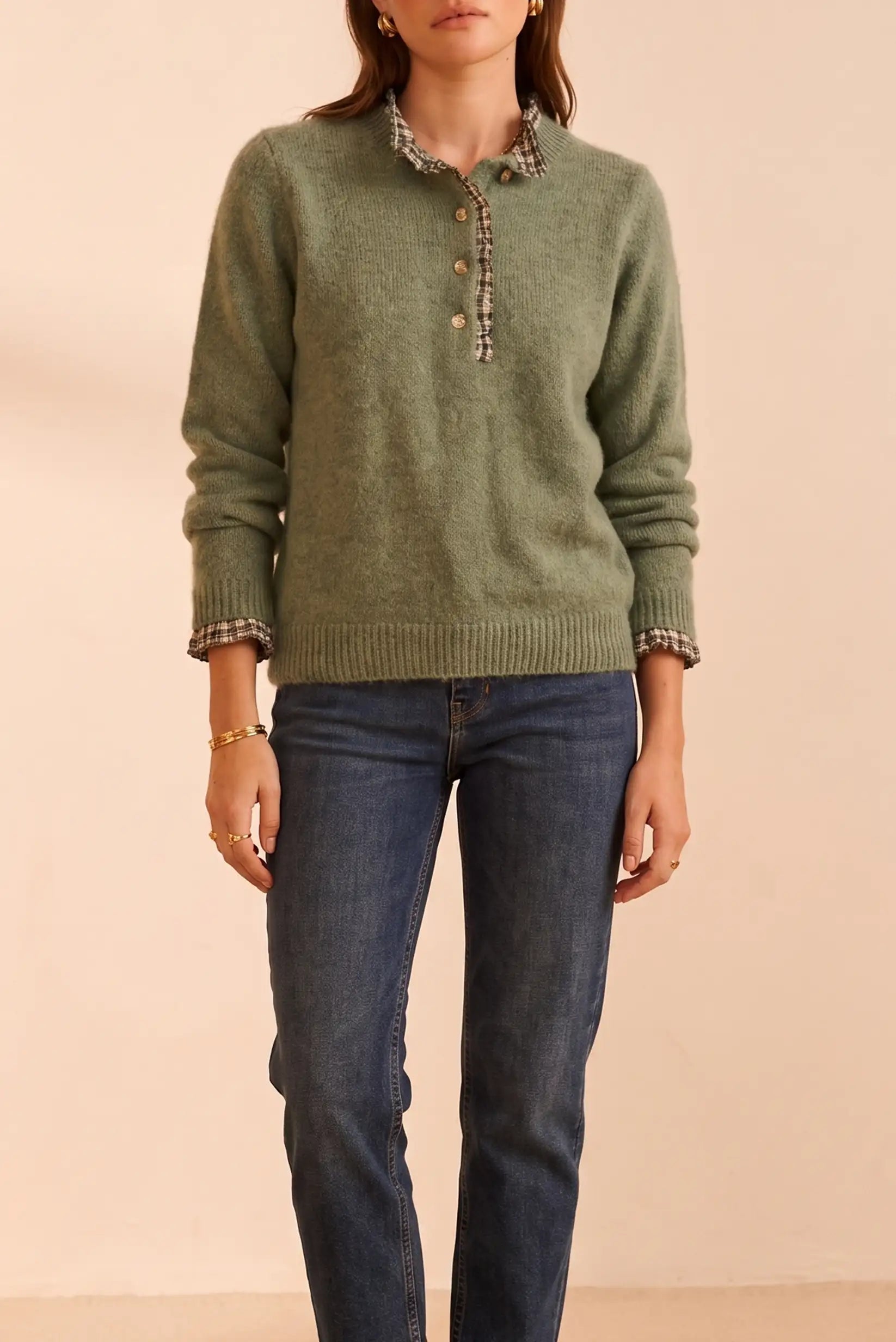 Suéter verde con cuello y puños a cuadros, botones dorados y jeans azules. Moda femenina cómoda y elegante.