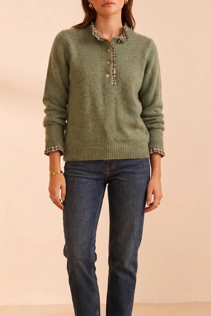 Suéter verde con cuello y puños a cuadros, botones dorados y jeans azules. Moda femenina cómoda y elegante.