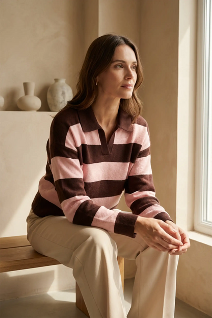 Mujer con jersey polo de manga larga a rayas rosas y marrones, sentada junto a ventana