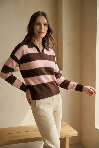 Mujer con jersey polo de manga larga a rayas rosas y marrones, pantalones beige, en interior minimalista