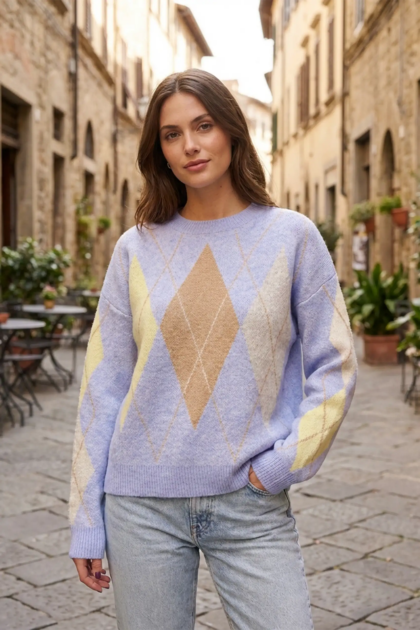 Mujer con jersey de rombos azul y beige, estilo casual CHICA del Sur, en calle adoquinada.