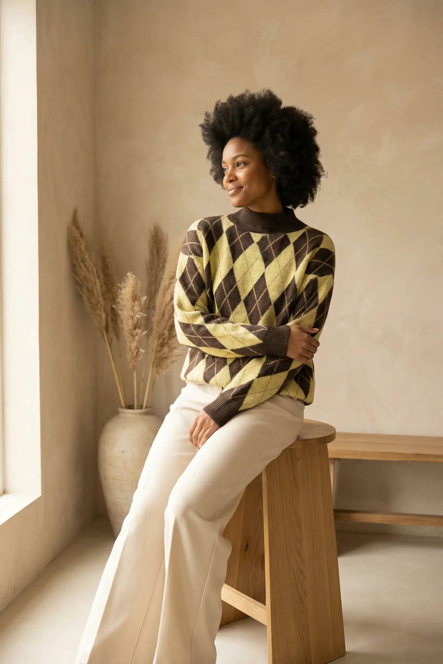 Mujer con jersey de rombos amarillo y marrón sentada en taburete de madera en interior minimalista
