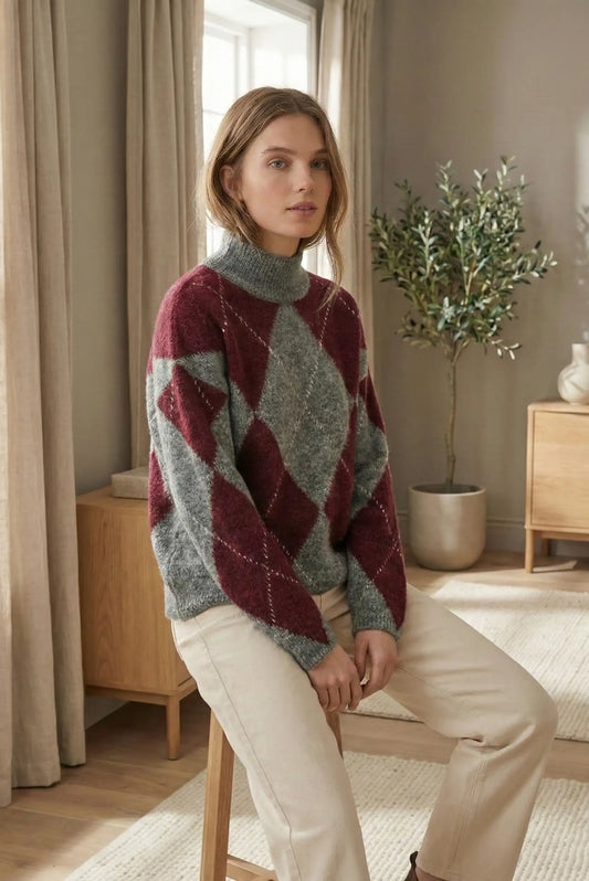 Mujer con jersey de rombos burdeos y gris sentada en taburete en sala con planta y muebles de madera