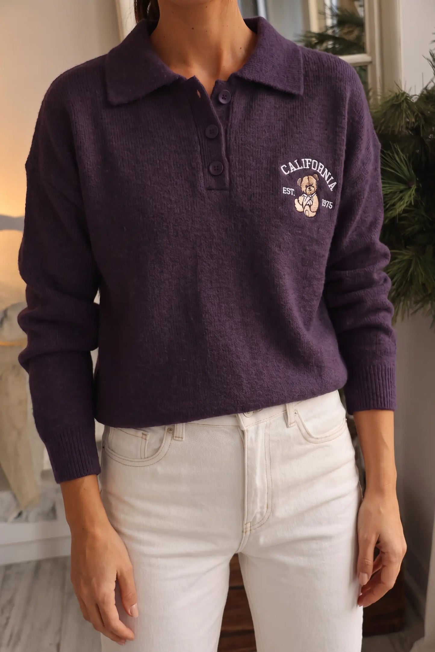 Mujer vistiendo jersey morado de punto con cuello polo y bordado de oso